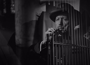Movie still from “The Asphalt Jungle” (1950), directed by John Huston – A man in a suit and a hat standing next to a metal cage; Close Up shot, Low angle