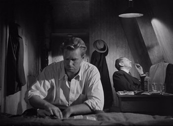 Movie still from “The Asphalt Jungle” (1950), directed by John Huston – A man sitting on a bed next to another man in a room; Medium shot, Low angle