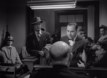 Movie still from “The Asphalt Jungle” (1950), directed by John Huston – A man in a suit and tie in front of another man in a suit and tie in front of another man in a suit and tie; Medium shot, Over the shoulder angle