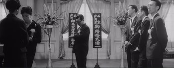 Movie still from “The Bad Sleep Well” (1960), directed by Akira Kurosawa – A black and white photo of a man standing in front of a window; Medium shot, Low angle