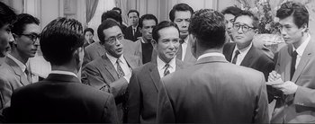Movie still from “The Bad Sleep Well” (1960), directed by Akira Kurosawa – A black and white photo of a group of men in business suits; Medium shot, Over the shoulder angle