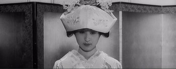 Movie still from “The Bad Sleep Well” (1960), directed by Akira Kurosawa – A woman wearing a hat with flowers on top of her head; Close Up shot, Low angle