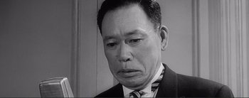 Movie still from “The Bad Sleep Well” (1960), directed by Akira Kurosawa – An older man in a suit and tie looking at the camera; Close Up shot, Low angle