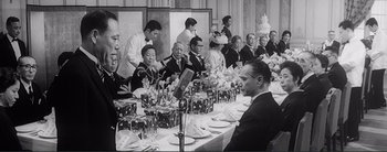 Movie still from “The Bad Sleep Well” (1960), directed by Akira Kurosawa – A group of people sitting at a long table; Medium shot, Over the shoulder angle
