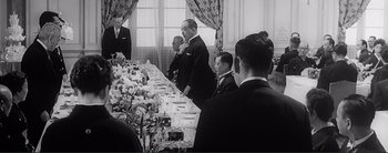 Movie still from “The Bad Sleep Well” (1960), directed by Akira Kurosawa – A black and white photo of people at a table; Medium shot, Over the shoulder angle