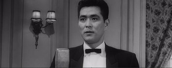 Movie still from “The Bad Sleep Well” (1960), directed by Akira Kurosawa – A black and white photo of a man in a suit and bow tie; Close Up shot, Low angle