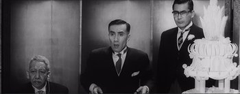 Movie still from “The Bad Sleep Well” (1960), directed by Akira Kurosawa – A man wearing a suit and tie in a room; Medium shot, Low angle