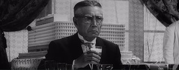 Movie still from “The Bad Sleep Well” (1960), directed by Akira Kurosawa – An older man in a suit and tie holding a glass of milk; Close Up shot, Low angle