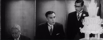 Movie still from “The Bad Sleep Well” (1960), directed by Akira Kurosawa – A black and white photo of a man in a suit and tie; Medium shot, Low angle