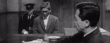 Movie still from “The Bad Sleep Well” (1960), directed by Akira Kurosawa – A man sitting at a table in front of another man; Medium shot, Over the shoulder angle