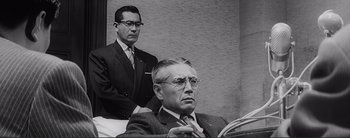 Movie still from “The Bad Sleep Well” (1960), directed by Akira Kurosawa – A man in a suit and tie next to another man in a suit and tie; Medium shot, Low angle