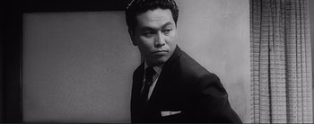 Movie still from “The Bad Sleep Well” (1960), directed by Akira Kurosawa – Black and white photograph of a man wearing a suit and tie; Close Up shot, Low angle