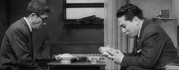 Movie still from “The Bad Sleep Well” (1960), directed by Akira Kurosawa – A black and white photo of a man playing a video game; Medium shot, Low angle