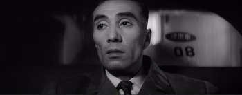 Movie still from “The Bad Sleep Well” (1960), directed by Akira Kurosawa – A black and white photo of a man in a suit and tie; Close Up shot, Low angle