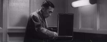 Movie still from “The Bad Sleep Well” (1960), directed by Akira Kurosawa – A black and white photo of a man working on a laptop computer; Medium shot, Low angle
