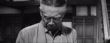 Movie still from “The Bad Sleep Well” (1960), directed by Akira Kurosawa – An older man with glasses is looking down; Close Up shot, Low angle