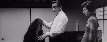 Movie still from “The Bad Sleep Well” (1960), directed by Akira Kurosawa – A black and white photo of a man holding a suit jacket; Medium shot, Low angle