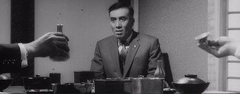 Movie still from “The Bad Sleep Well” (1960), directed by Akira Kurosawa – A black and white photo of a man sitting at a table; Close Up shot, Low angle