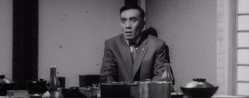 Movie still from “The Bad Sleep Well” (1960), directed by Akira Kurosawa – A man sitting at a table in front of a wall; Medium shot, Low angle
