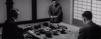 Movie still from “The Bad Sleep Well” (1960), directed by Akira Kurosawa – A black and white photo of a man in a suit sitting on the floor; Medium shot, High angle