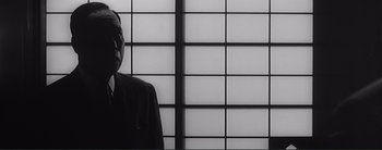 Movie still from “The Bad Sleep Well” (1960), directed by Akira Kurosawa – A man standing in front of a wall with a window behind him; Close Up shot, Low angle