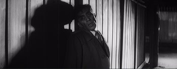 Movie still from “The Bad Sleep Well” (1960), directed by Akira Kurosawa – A man wearing a suit and tie standing in front of a wall; Medium shot, Low angle