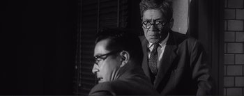 Movie still from “The Bad Sleep Well” (1960), directed by Akira Kurosawa – A man and a man in a suit and tie; Medium shot, Over the shoulder angle