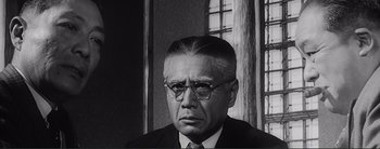 Movie still from “The Bad Sleep Well” (1960), directed by Akira Kurosawa – An older man wearing glasses and a suit and tie; Close Up shot, Low angle