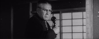 Movie still from “The Bad Sleep Well” (1960), directed by Akira Kurosawa – An older man in a suit and tie holding a phone; Close Up shot, Low angle