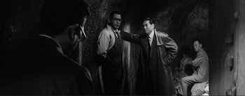 Movie still from “The Bad Sleep Well” (1960), directed by Akira Kurosawa – A man pointing at another man wearing a suit; Medium shot, Over the shoulder angle