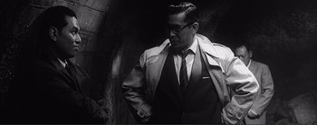 Movie still from “The Bad Sleep Well” (1960), directed by Akira Kurosawa – A black and white photo of a man wearing a suit and tie; Medium shot, Low angle