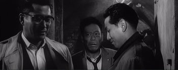 Movie still from “The Bad Sleep Well” (1960), directed by Akira Kurosawa – A group of men standing next to each other in a room; Medium shot, Over the shoulder angle