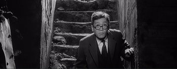 Movie still from “The Bad Sleep Well” (1960), directed by Akira Kurosawa – A man in a suit and tie sitting on a staircase; Medium shot, Low angle