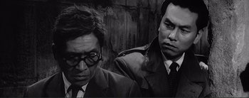 Movie still from “The Bad Sleep Well” (1960), directed by Akira Kurosawa – A black - and - white photo of two men sitting next to each other; Close Up shot, Over the shoulder angle