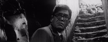 Movie still from “The Bad Sleep Well” (1960), directed by Akira Kurosawa – A man in a suit and tie wearing glasses; Close Up shot, Low angle