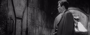 Movie still from “The Bad Sleep Well” (1960), directed by Akira Kurosawa – A black and white photo of a man looking at a wall; Medium shot, Over the shoulder angle