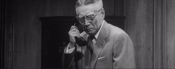 Movie still from “The Bad Sleep Well” (1960), directed by Akira Kurosawa – An older man wearing a suit and tie while holding a phone to his ear; Medium shot, Low angle