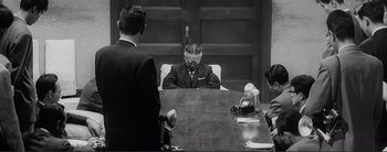 Movie still from “The Bad Sleep Well” (1960), directed by Akira Kurosawa – A man sitting in front of another man at a table; Medium shot, High angle