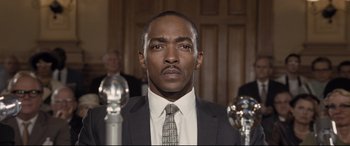 Movie still from “The Banker” (2020), directed by George Nolfi – A man wearing a suit and tie in front of a group of people; Close Up shot, Low angle