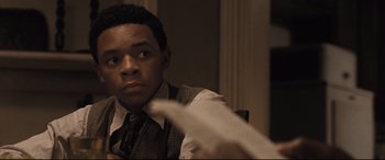 Movie still from “The Banker” (2020), directed by George Nolfi – A man sitting at a table holding a piece of paper in front of him; Close Up shot, Over the shoulder angle