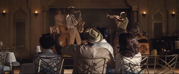 Movie still from “The Banker” (2020), directed by George Nolfi – A group of men playing musical instruments on a stage; Extreme Wide shot, Over the shoulder angle