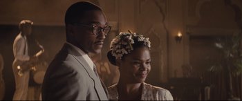 Movie still from “The Banker” (2020), directed by George Nolfi – A man standing next to a woman wearing a flower crown; Close Up shot, Over the shoulder angle