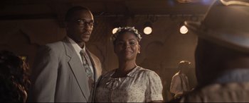 Movie still from “The Banker” (2020), directed by George Nolfi – A man and a woman standing next to each other in front of lights; Medium shot, Over the shoulder angle