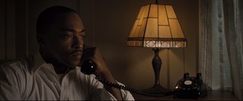 Movie still from “The Banker” (2020), directed by George Nolfi – A man talking on a phone in front of a lamp; Close Up shot, High angle