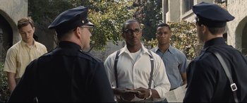 Movie still from “The Banker” (2020), directed by George Nolfi – A man in a white shirt is holding a book; Medium shot, Over the shoulder angle