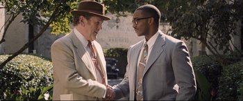 Movie still from “The Banker” (2020), directed by George Nolfi – Two men in suits shaking hands in front of a building; Medium shot, Over the shoulder angle
