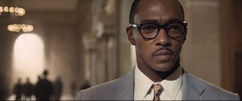Movie still from “The Banker” (2020), directed by George Nolfi – A person wearing glasses and a suit; Close Up shot, Low angle