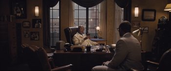 Movie still from “The Banker” (2020), directed by George Nolfi – A man sitting at a desk in front of a woman; Medium shot, Over the shoulder angle