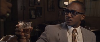 Movie still from “The Banker” (2020), directed by George Nolfi – A man sitting in a chair holding a glass of wine; Close Up shot, Over the shoulder angle