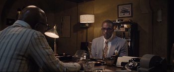 Movie still from “The Banker” (2020), directed by George Nolfi – A man sitting at a table in front of a woman; Medium shot, Over the shoulder angle